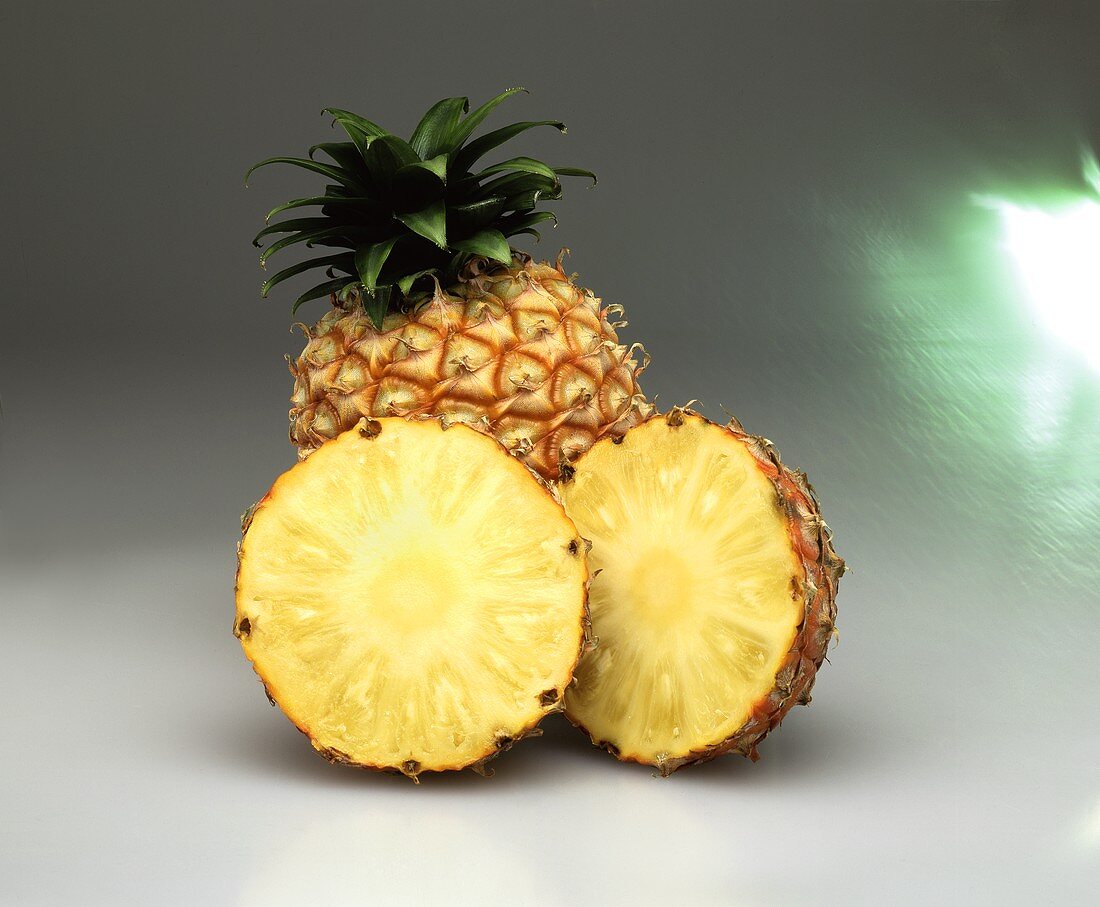Two pineapple halves in front of a pineapple