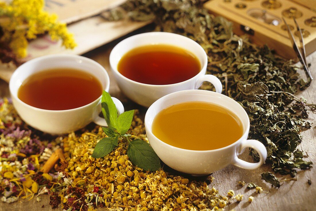 Three medicinal teas in cups with dried medicinal herbs