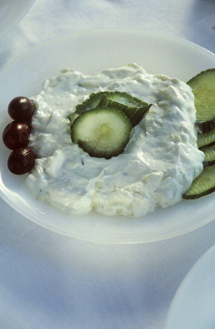 Tzaziki with sliced cucumber and olives on a white plate