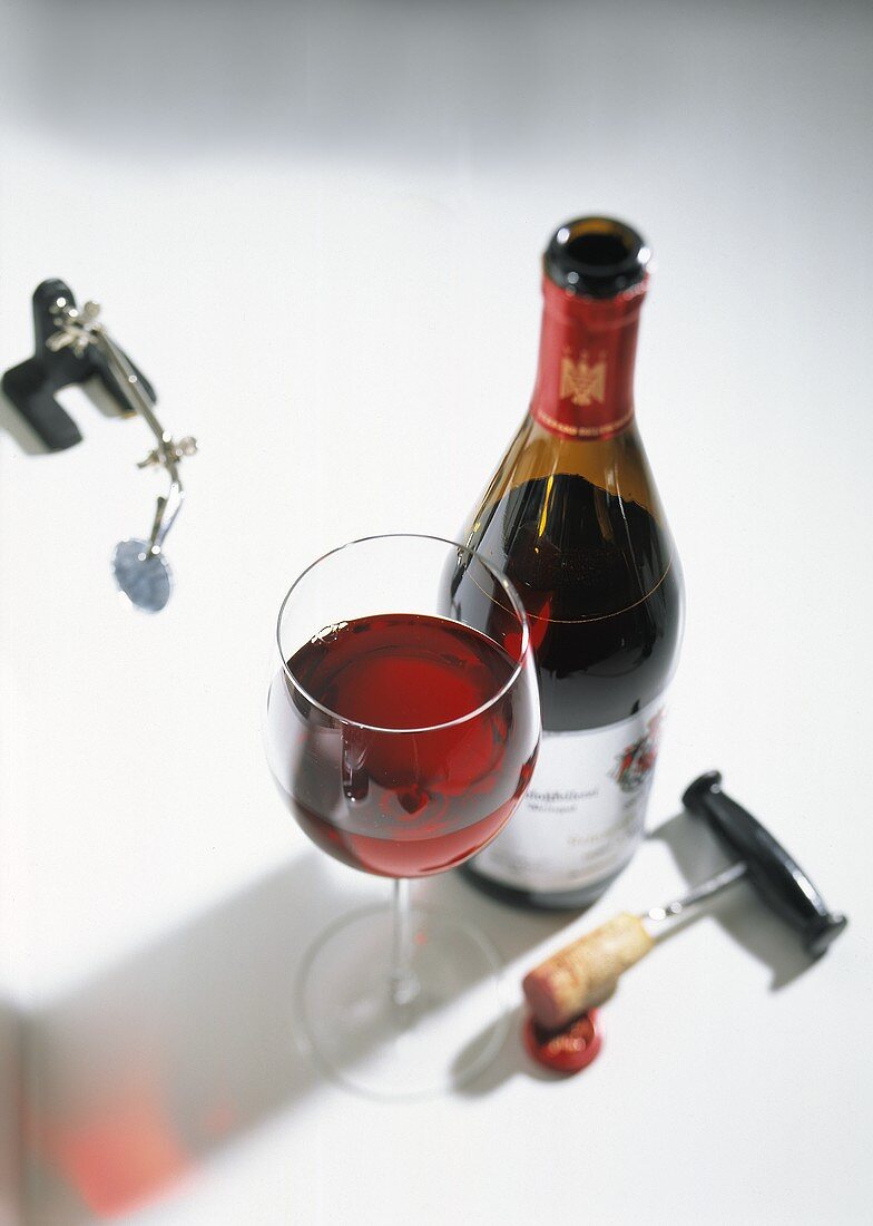 Rotwein in Flasche und Glas, daneben ein Korkenzieher