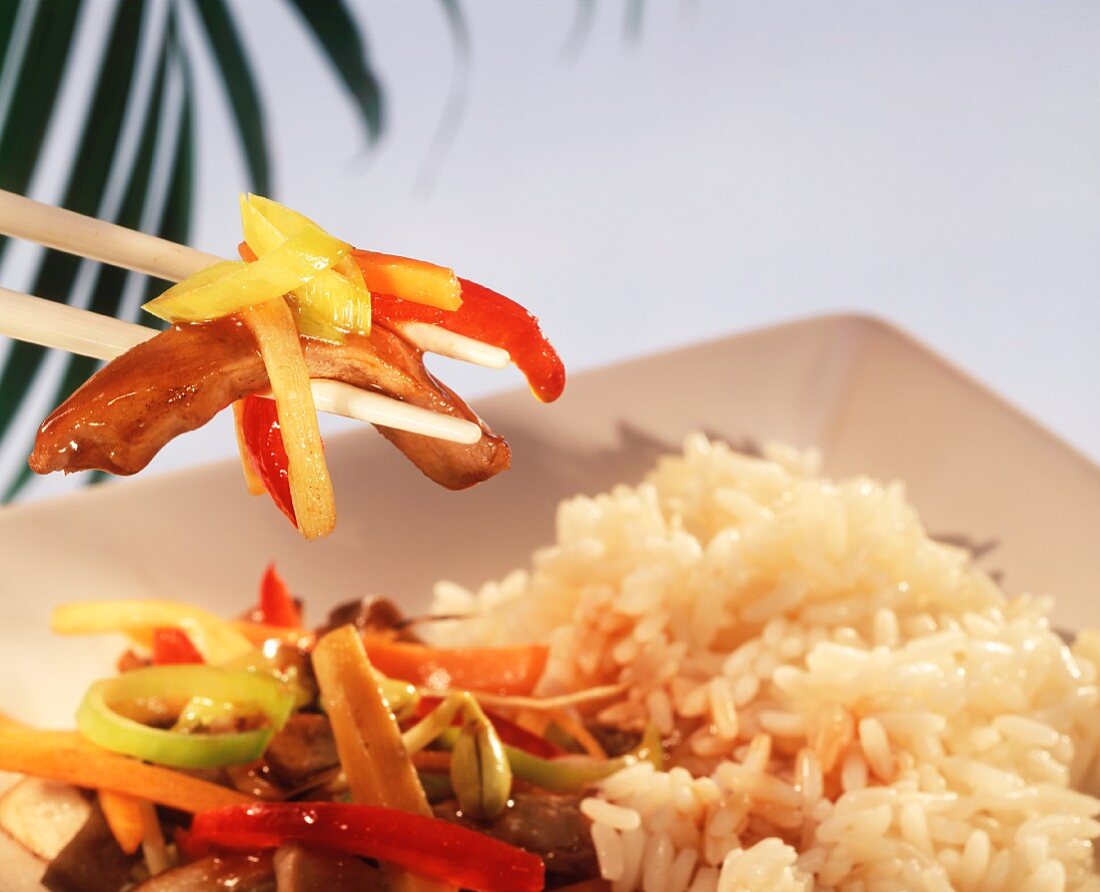 Chop suey with pork on chopsticks above plate