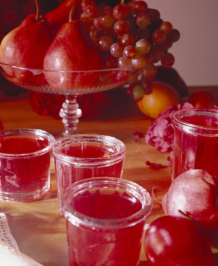 Red jam in jars in front of a fruit bowl