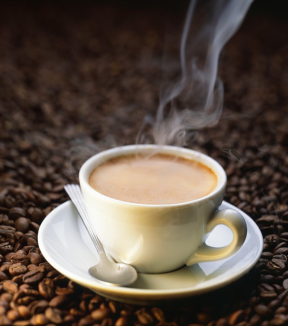 A steaming cup of coffee on coffee beans