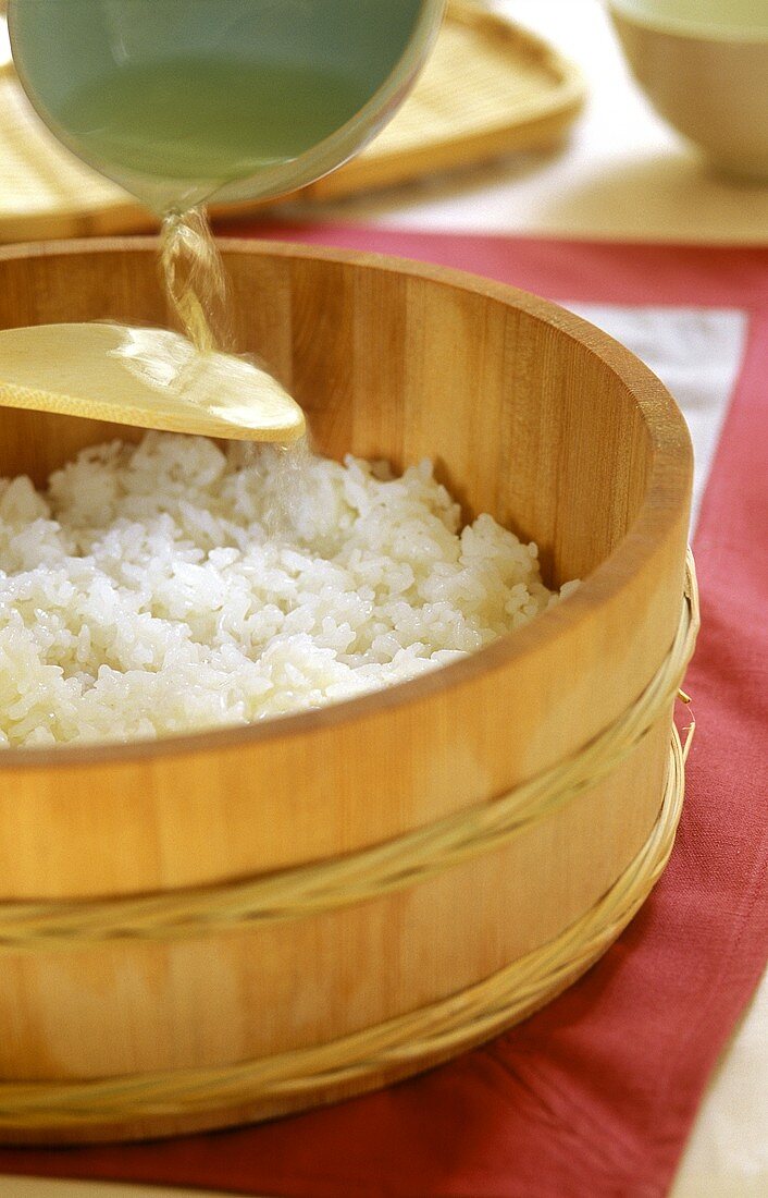 Reisessig über Löffel in Reis gießen