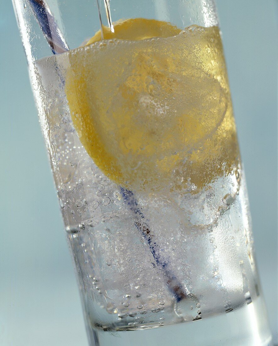 Wasser in Glas mit Zitronenscheibe gießen