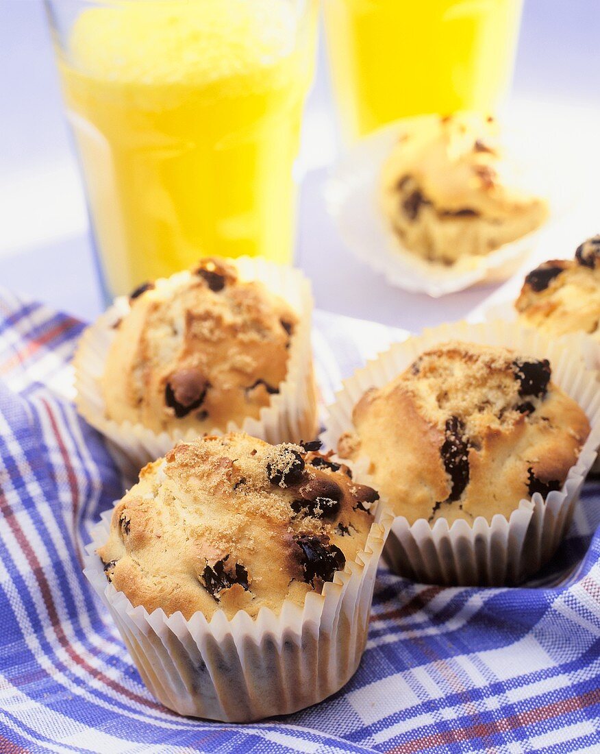 Muffins in Papierförmchen vor Orangensaftgläsern