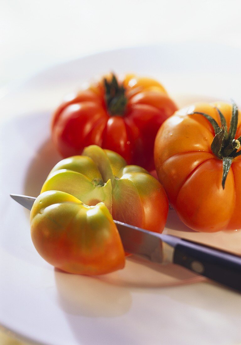 Three beefsteak tomatoes, one sliced, with knife