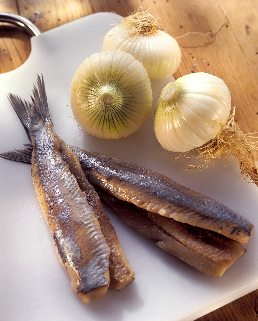 Two herrings without heads with onions on chopping board