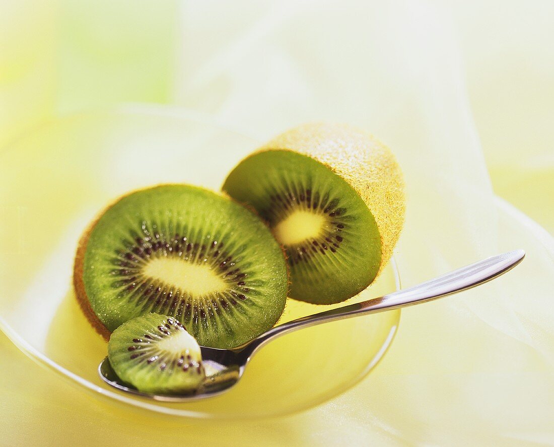 Two kiwi fruit halves & piece of kiwi fruit on spoon in a bowl