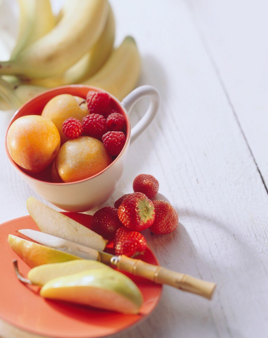 Verschiedene Obstsorten mit Beeren auf Teller und in Tasse