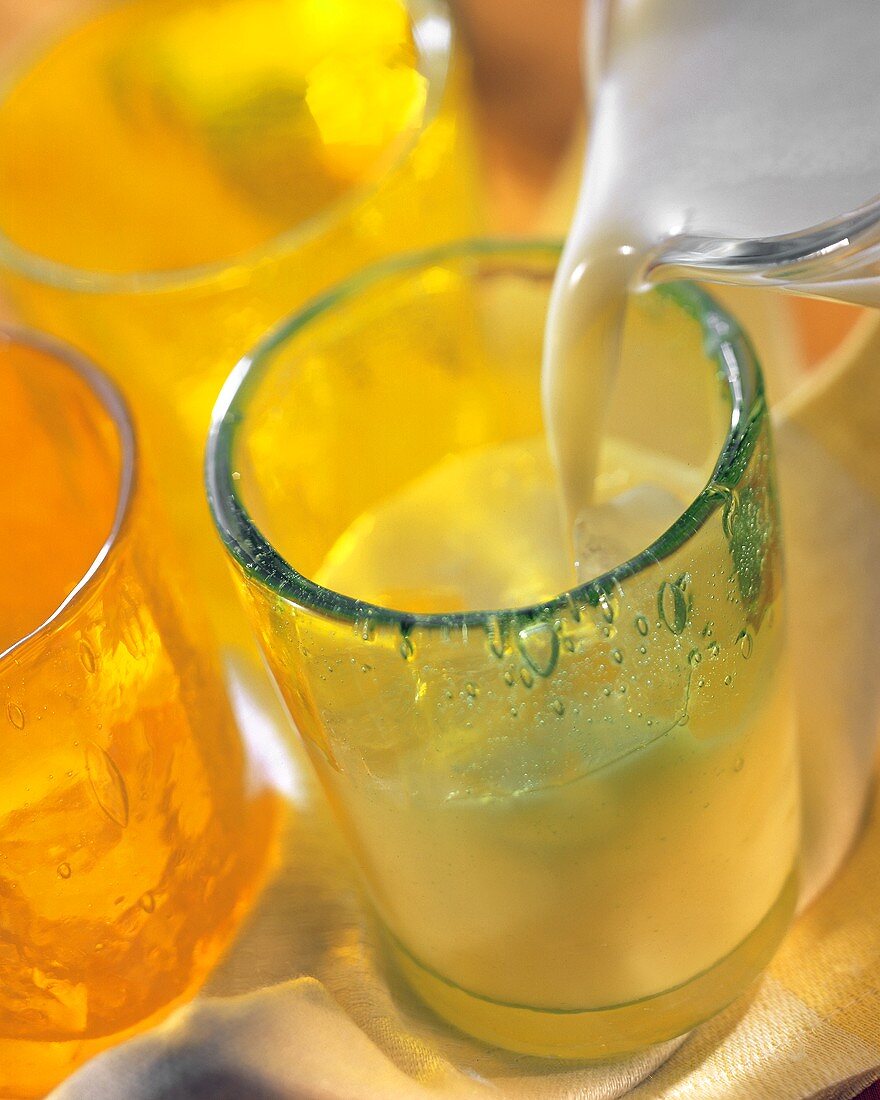 Pouring pineapple & almond shake into glass of crushed ice