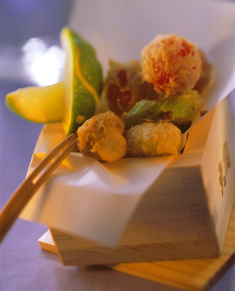 Vegetable tempura in wooden box with wedge of lime