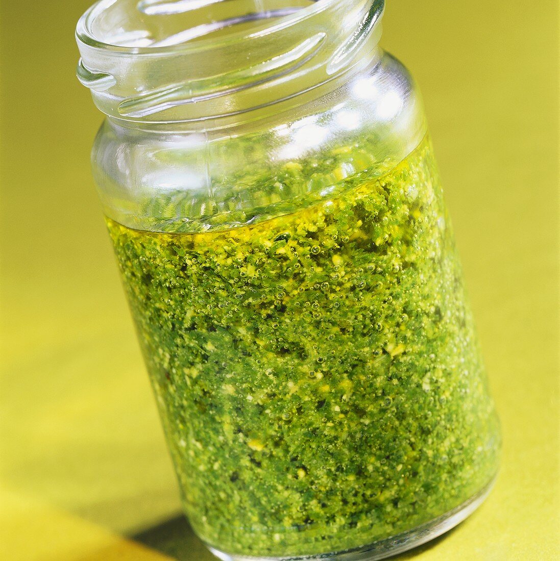 Pesto in an open jar on pale green background