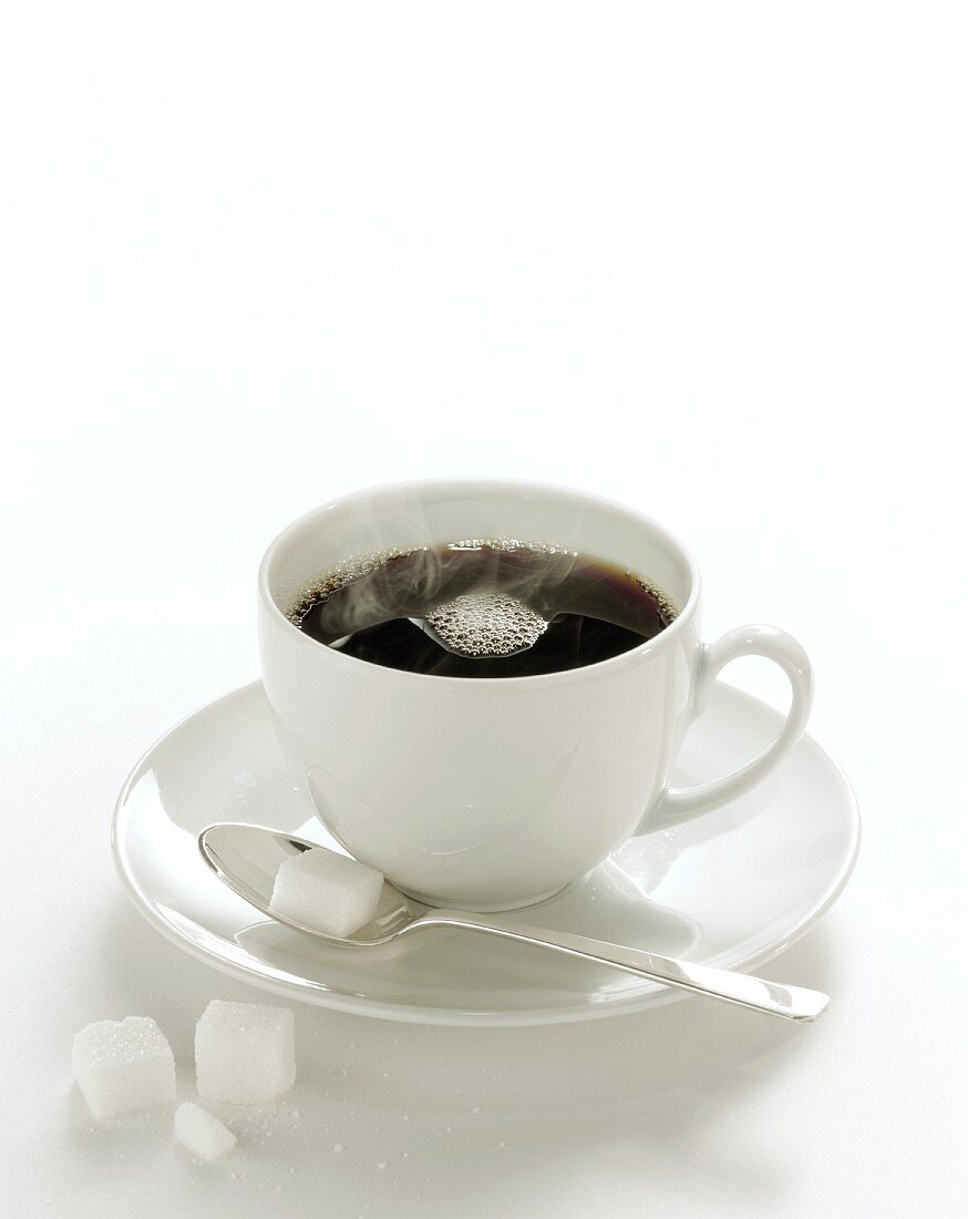 Steaming black coffee in white cup; sugar cube