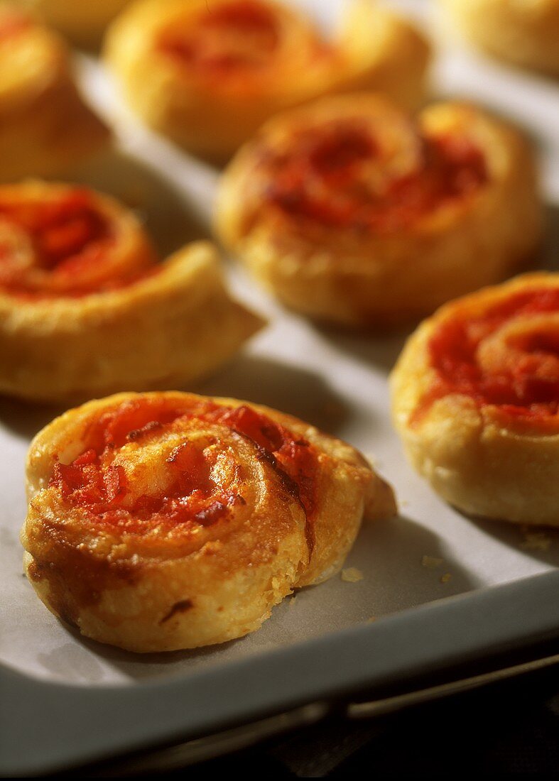 Puff pastry snails with ham and tomatoes on baking sheet