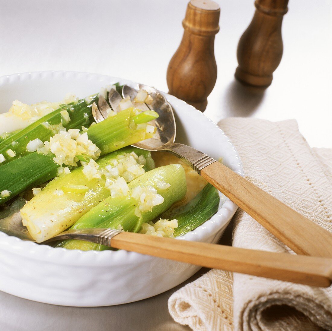 Leeks in sherry with onions in a bowl with salad servers
