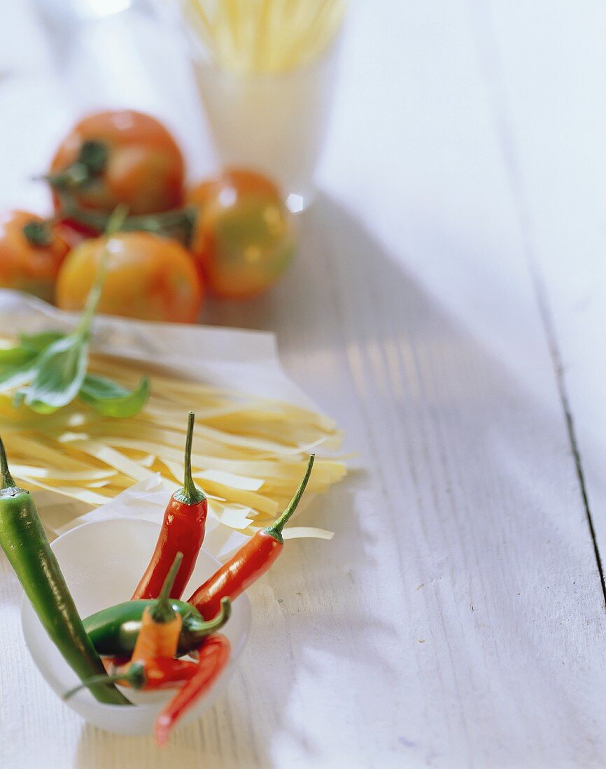 Stillleben mit Chilischoten, Bandnudeln, Tomaten und Basilikum