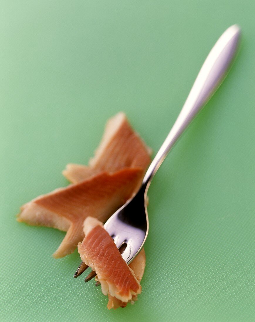 Smoked trout fillet with fork on green background