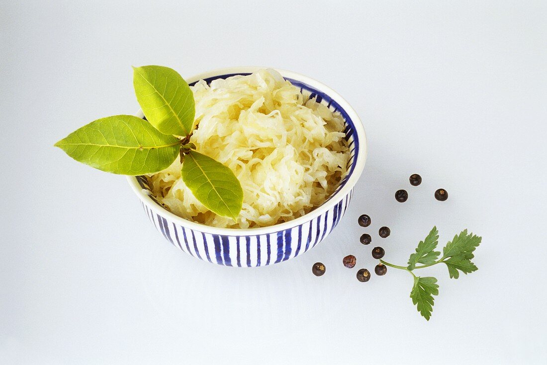 Sauerkraut mit Lorbeerzweig in Schüssel; Wacholderbeeren