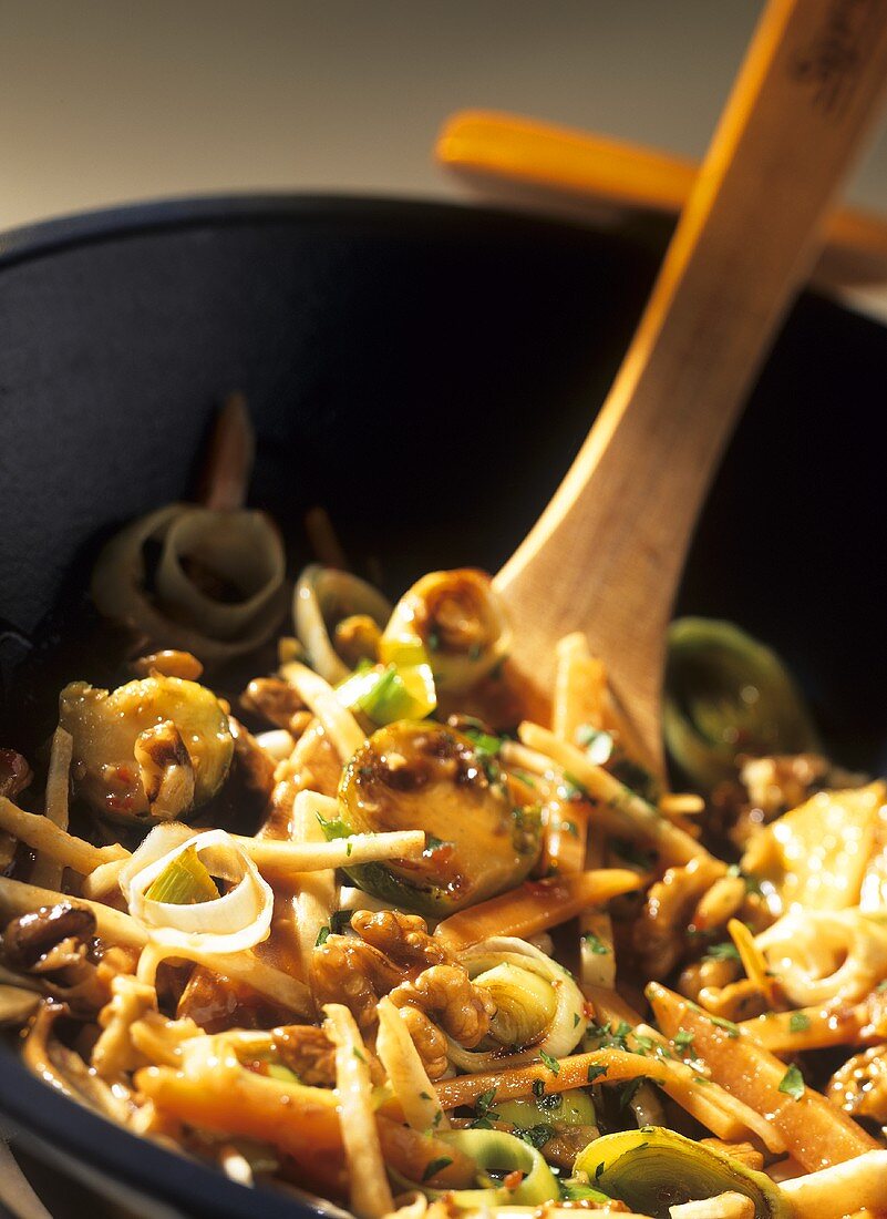 Sweet & sour winter vegetables & walnuts in wok, wooden spoon