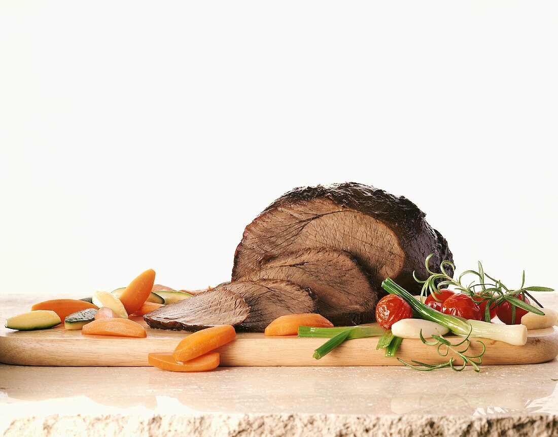 Roast beef with cooked vegetables on chopping board