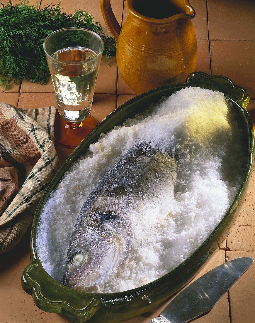 Ganzer Seebarsch in Salzkruste; Weissweinglas; Krug