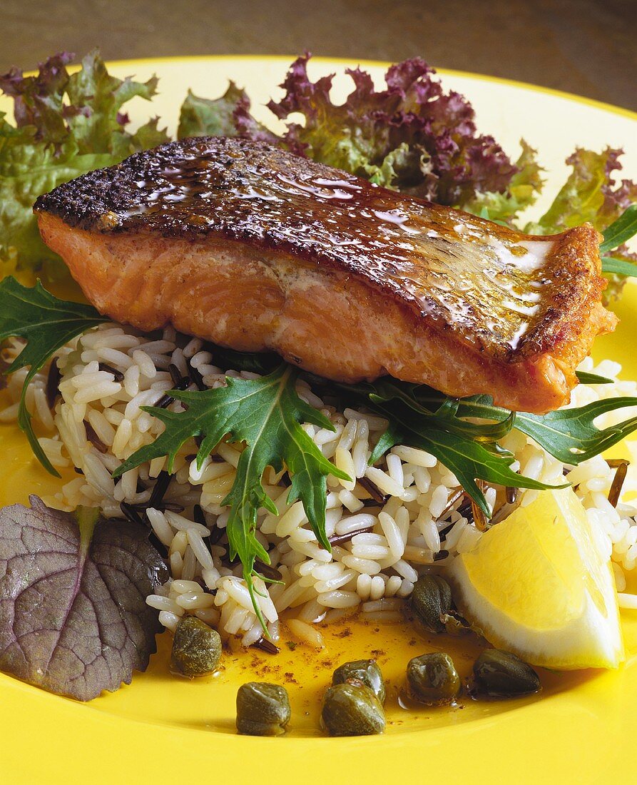 Fried salmon on rice with capers and lemon wedge
