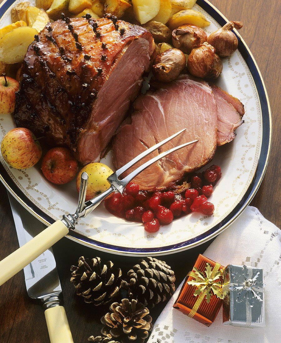 Glazed ham on a platter with cranberries, apples etc