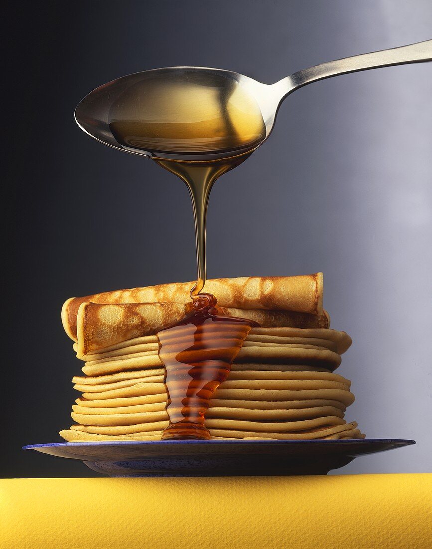 Maple Syrup Dripping from Spoon Onto Plate of Pancakes