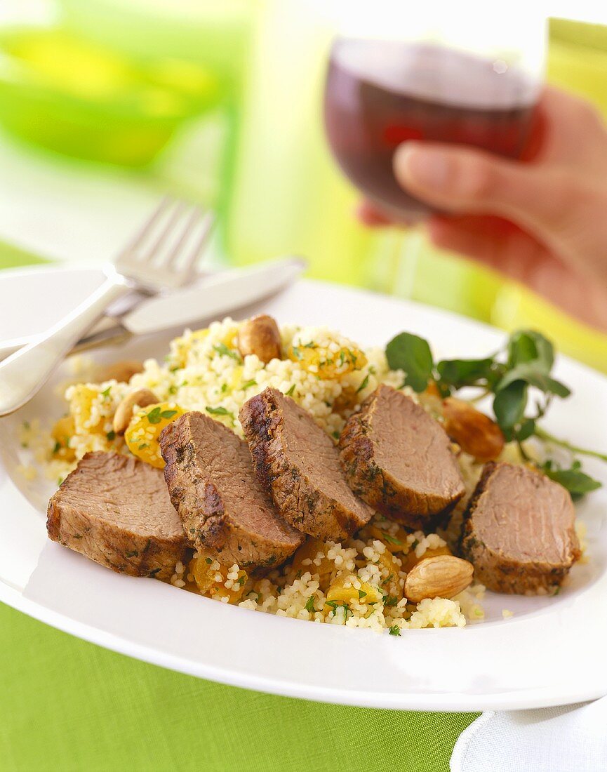 Sliced roast beef on couscous; hand with red wine glass