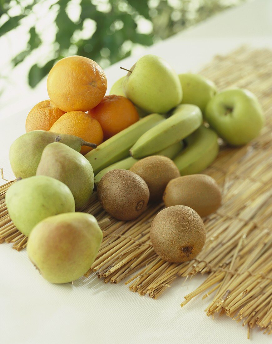 Kiwis, bananas, oranges, apples and pears on straw mat