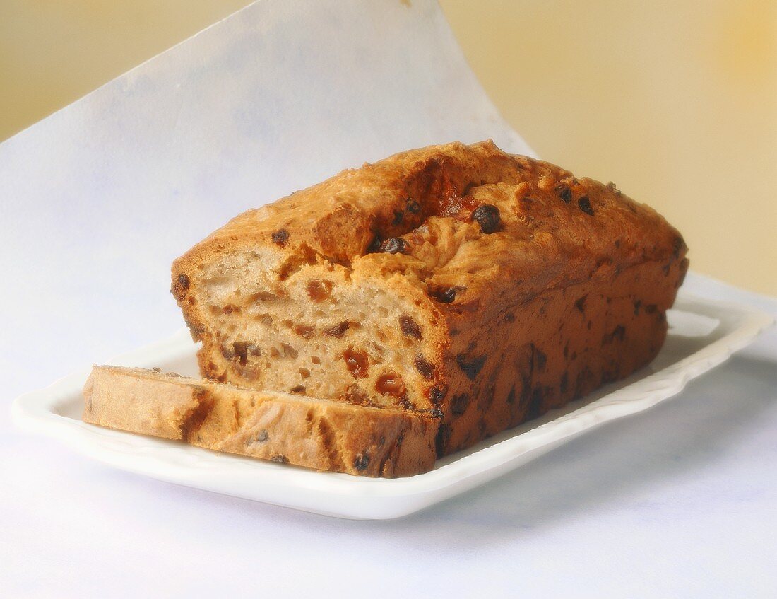 Fruit loaf with raisins, a slice cut, on white plate