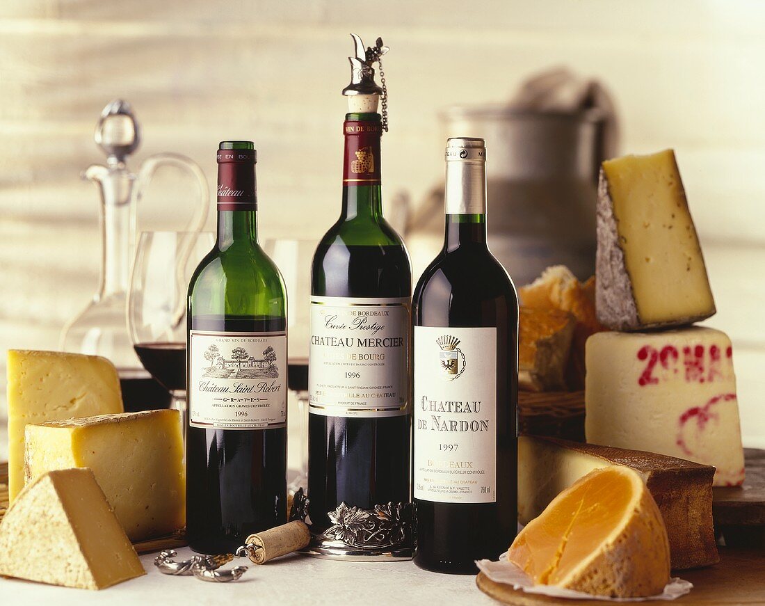 Various types of cheese and three red wine bottles