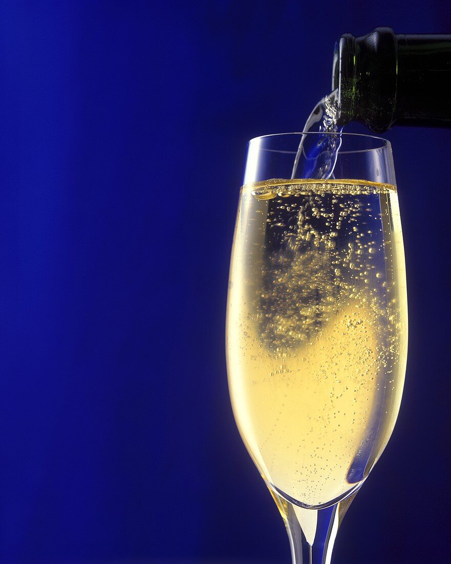 Pouring champagne into a glass against a dark blue backdrop