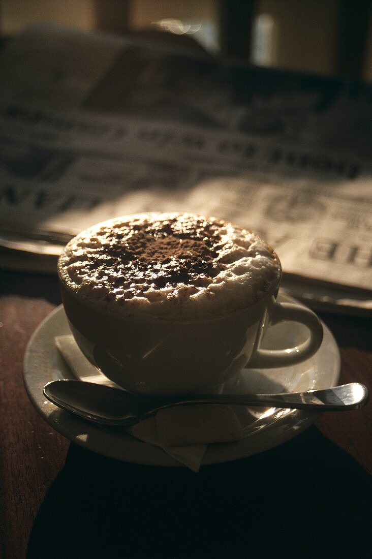 Eine Tasse Cappuccino vor einer Zeitung auf Tisch