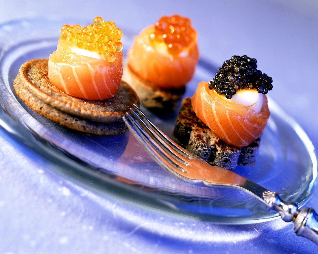 Canapés mit Lachs, Ei und drei Sorten Kaviar auf Teller