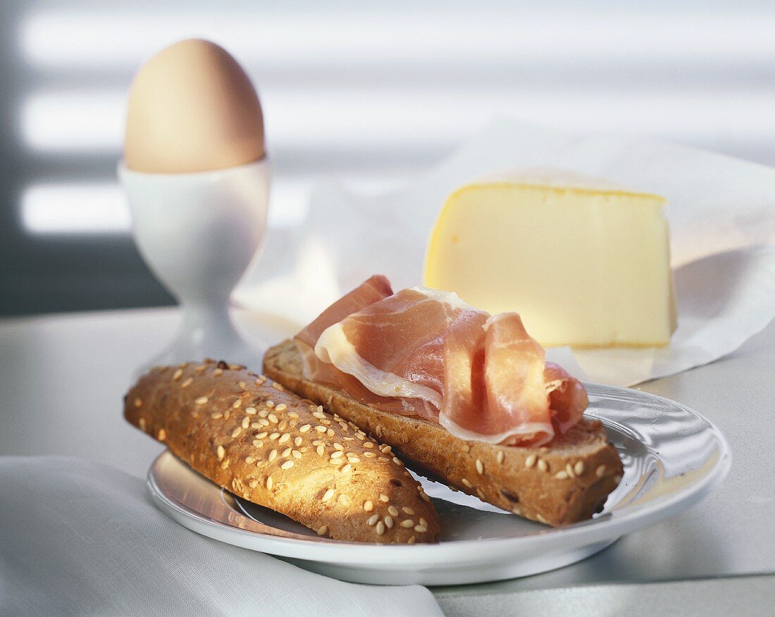 Schinkenbrötchen auf Teller, Ei im Eierbecher und Käse