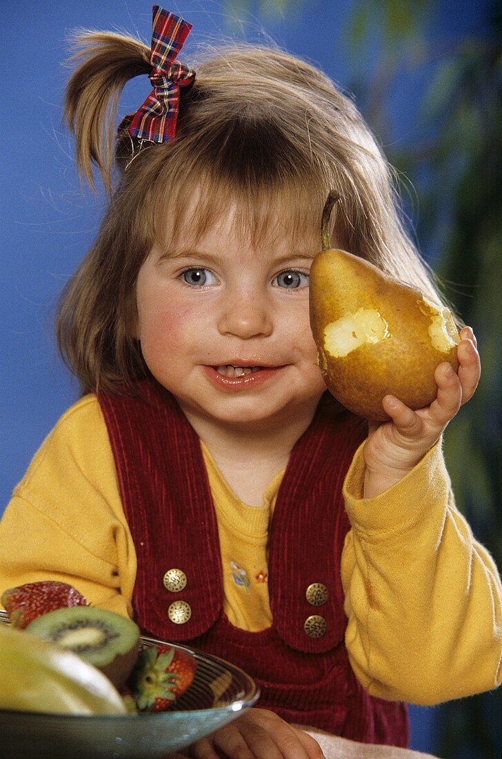Small girl with pear, with bite taken, in her hand