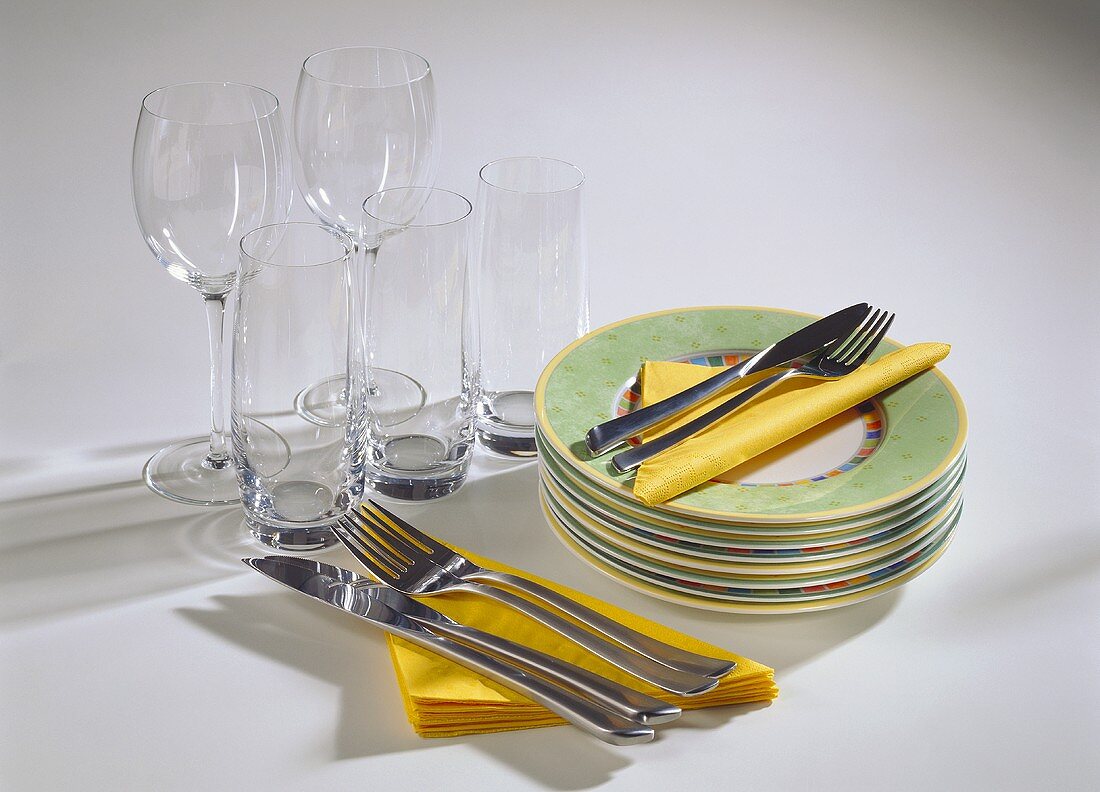 Glasses, pile of plates, cutlery & yellow paper napkins