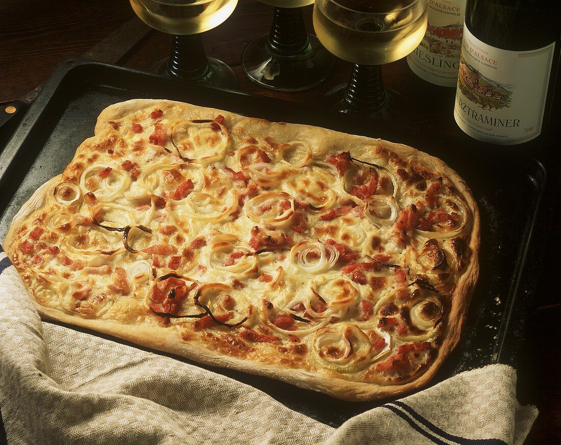 Alsatian pizza (Flammenkuchen) on baking sheet; white wine