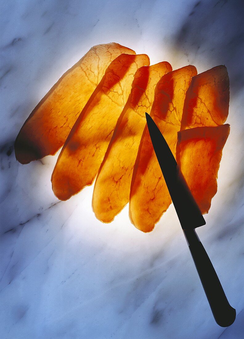 Slices of raw ham with a knife on a marble platter