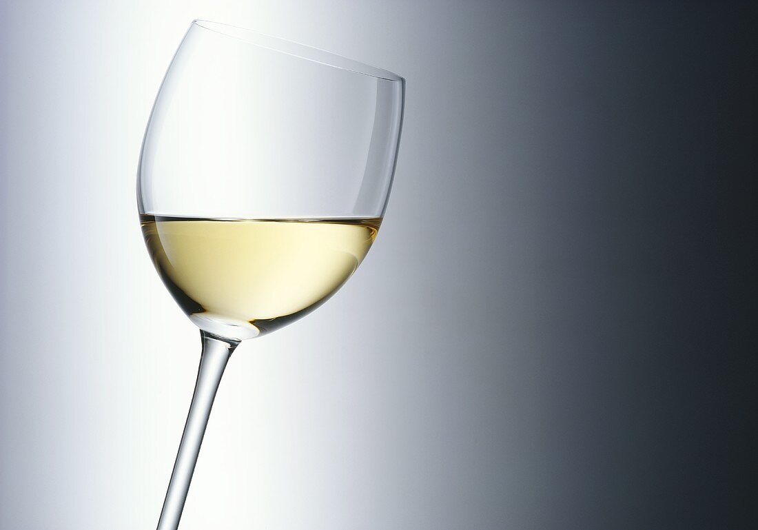A glass of white wine held at an angle