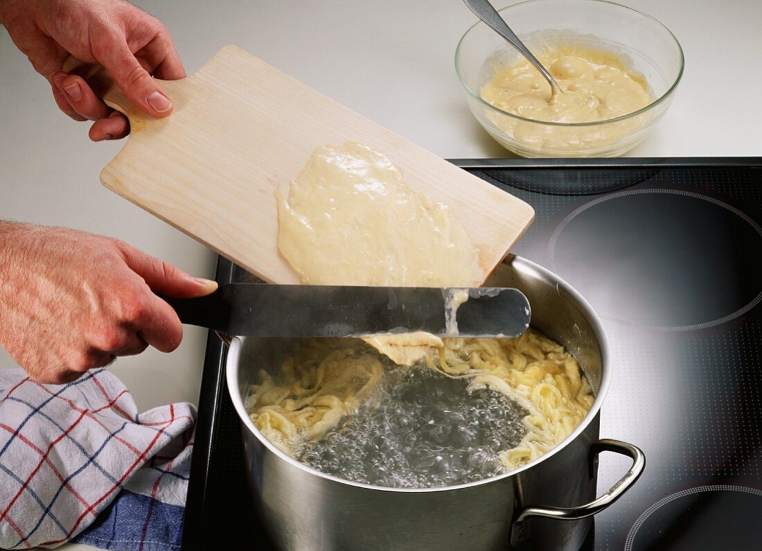 Making noodles (Spaetzle): scraping dough into boiling water