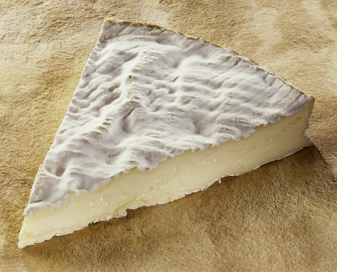 Ein Stück Brie de Meaux auf braunem Untergrund