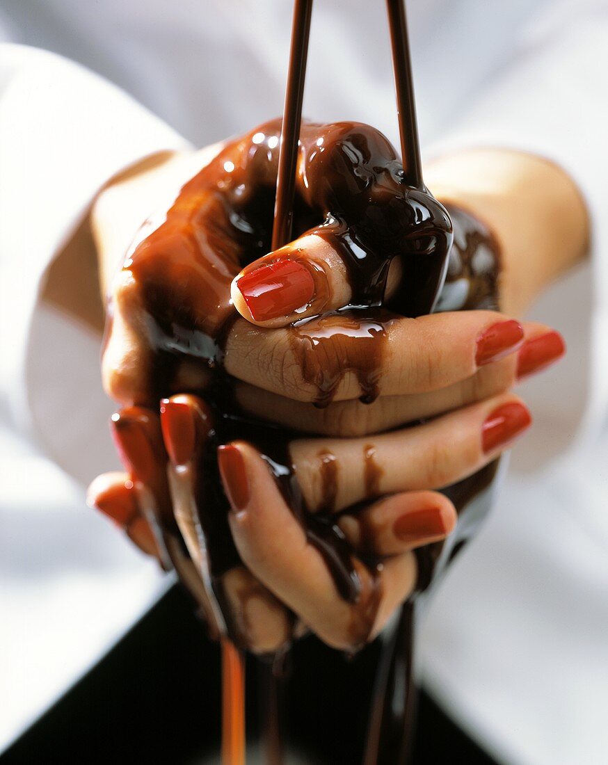 Chocolate sauce running over a woman's hands