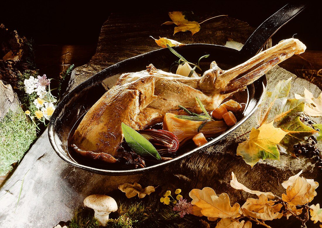 Leg of venison with vegetables in a pan; forest decoration