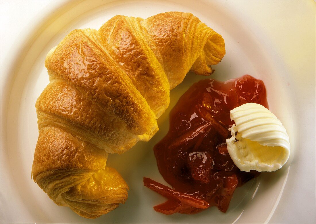 Croissant, jam and butter curl on a plate