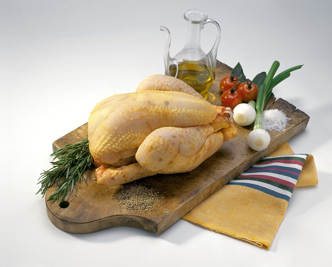 Whole chicken, vegetables, spices and oil on a chopping board