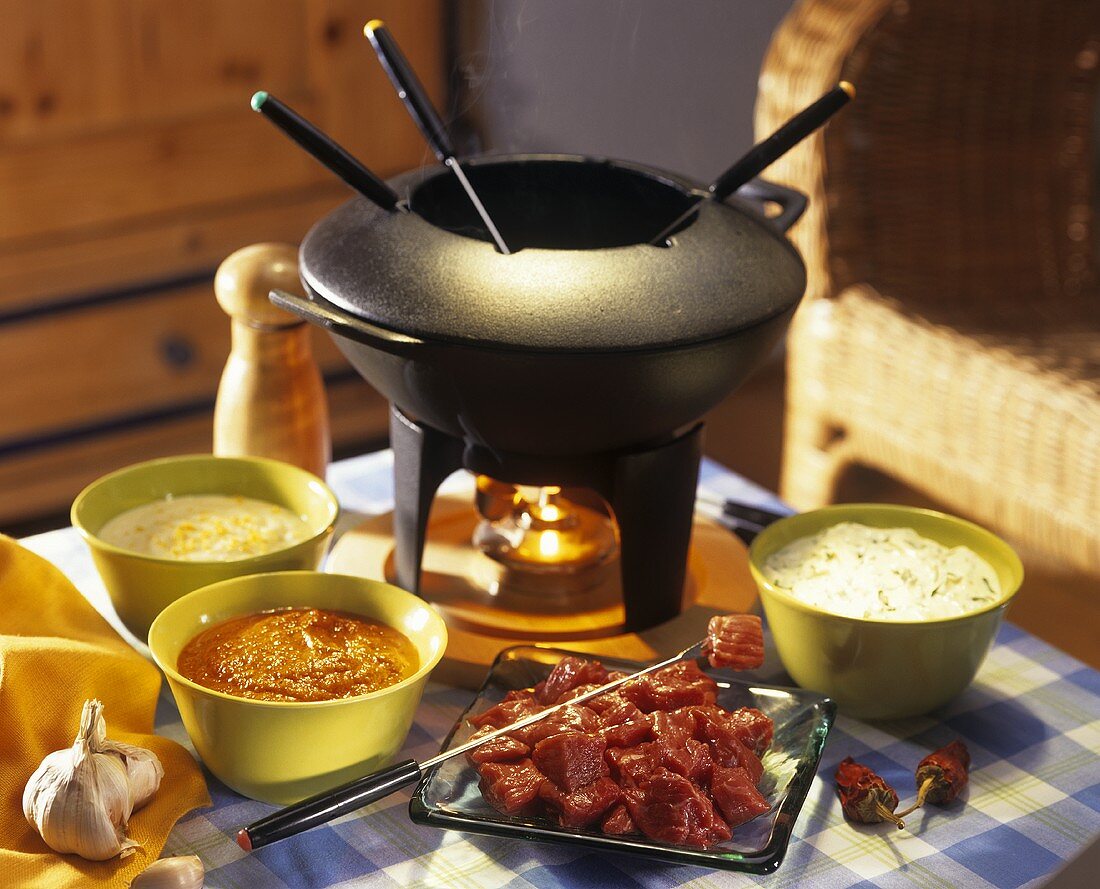 Meat fondue with three dips and fondue pot on a table