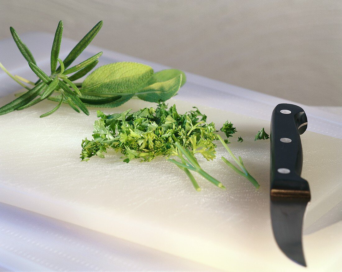 Various herbs, some chopped, on chopping board